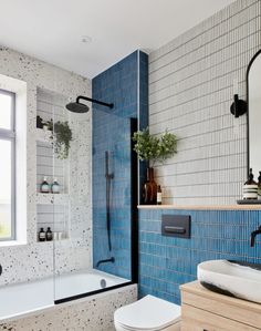 a bathroom with blue tiles and a white toilet sitting next to a bathtub in front of a window