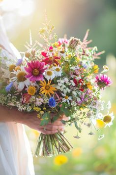 a woman holding a bouquet of wildflowers and daisies in her hands on a sunny day