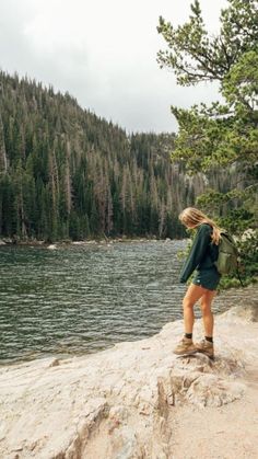 a woman standing on the edge of a cliff overlooking a body of water with trees in the background