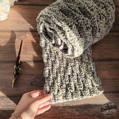 a woman's hand holding onto a knitted hat on top of a wooden table