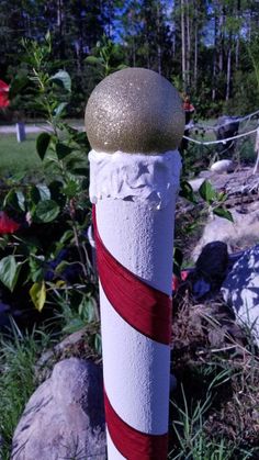 there is a white and red striped pole with a green top on the grass next to some rocks