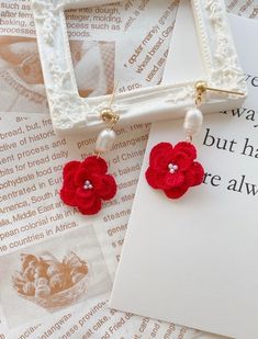 red crocheted flower and pearl drop earrings on top of an old book page