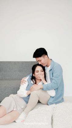 a man and woman sitting on top of a bed next to each other with their arms around one another