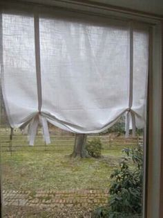 an open window with white curtains on the outside and trees in the yard behind it