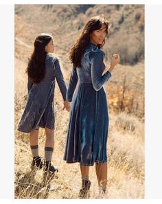 two women in blue dresses are walking through the grass and one is holding her hand