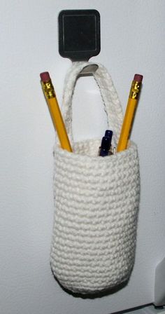 two pencils in a crochet bag hanging on the wall next to a cell phone