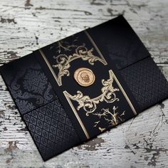 a black and gold wedding card with a button on the front is sitting on a table