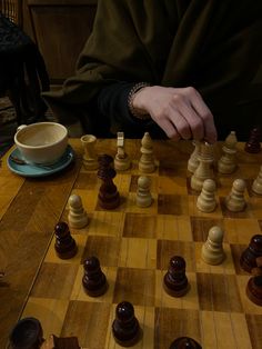 a person playing chess on a wooden table with a cup of coffee in the background