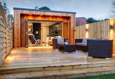 a wooden deck with chairs and lights on it next to a building that has a patio area