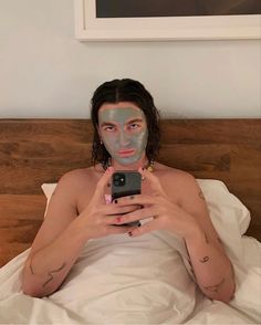 a man laying in bed with his face painted like a person holding a cell phone