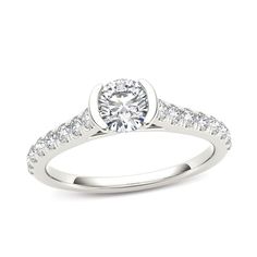 a white gold engagement ring with diamonds on the band and a round cut diamond in the center