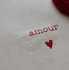 a red ball of yarn sitting on top of a white cloth with the word'amour'written across it