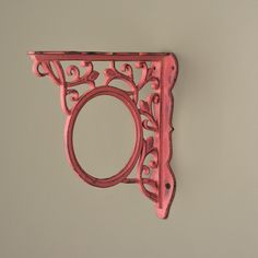 a pink metal object hanging from the side of a wall with an ornate design on it