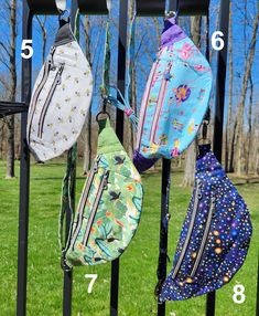 several purses hanging on a metal fence in the grass with numbers written below them