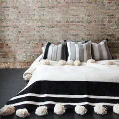 a black and white bed with pom poms on the bottom, in front of a brick wall