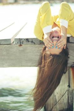 a woman with long hair laying down on a wooden dock next to the water and holding her head in her hands