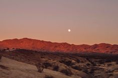 the moon is setting in the sky over mountains