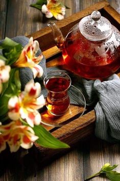 a glass tea pot and cup on a wooden tray with flowers