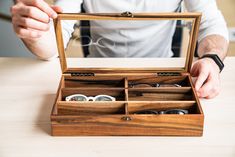 a man is holding an open wooden box with sunglasses in it and his hands are on the table