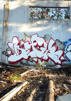 an old building with graffiti on the side and windows in the back ground, along with some weeds growing out of it