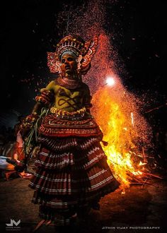 a woman dressed in traditional garb standing next to a fire