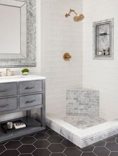 a bathroom with white walls and black tile flooring, two mirrors on the wall