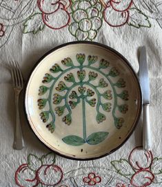 a plate with a flower design on it next to a fork and knife sitting on a tablecloth