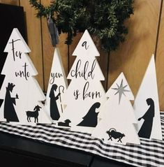 three wooden christmas trees with black and white silhouettes on them, one has a nativity scene