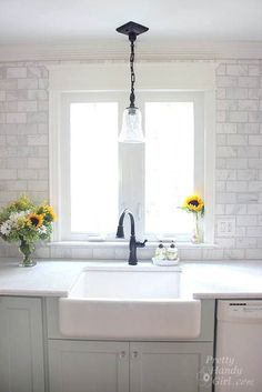 a white kitchen sink under a window with sunflowers in vases on the counter