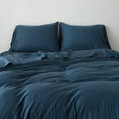 an unmade bed with blue sheets and pillows on it's headboard, against a white wall