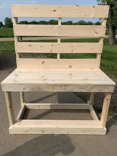 a bench made out of wooden planks sitting on top of a cement ground next to a field