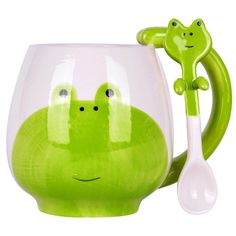 a green frog mug with a spoon in it's mouth and two faces on the handle