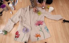 a woman sitting on the floor next to a piece of cloth with flowers painted on it