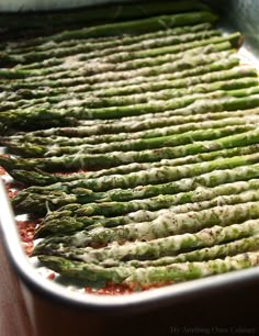 asparagus being cooked in a pan on a wooden table with red sauce and seasoning