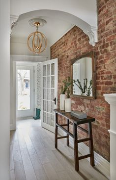 a room with a brick wall and wooden flooring next to a white door that has a mirror on it