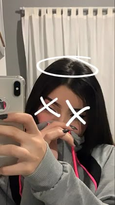 a woman taking a selfie with her cell phone in front of her head and two crosses drawn on it