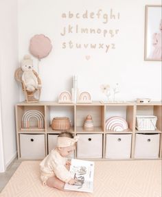 a baby sitting on the floor reading a book in front of a wall with letters