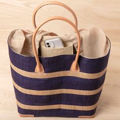 a blue and tan striped bag with a cell phone in the bottom pocket, sitting on a wooden surface