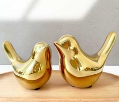 two golden bird figurines sitting on top of a wooden tray