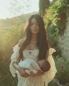 a woman holding a baby in her arms and wearing a white dress with ruffled sleeves