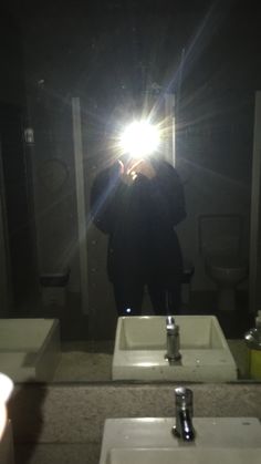 a person taking a selfie in front of two sinks with the light shining on them