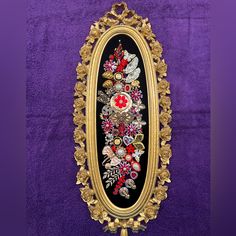 an ornate gold frame with flowers and leaves painted on it in black, red, yellow and purple