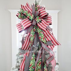 a christmas tree with red, white and green ribbons on it's bow is standing in front of a door