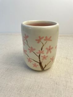 a white cup with pink flowers on it sitting on top of a cloth covered table