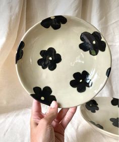 two black and white plates with flowers on them, one being held up by a hand