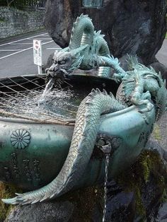 two green dragon statues sitting on the side of a fountain with water running from it