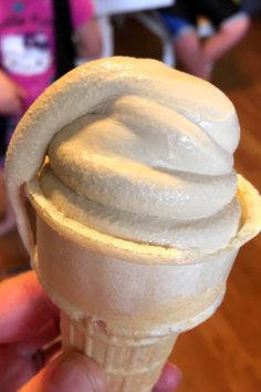 a hand holding an ice cream cone with white icing on it's top