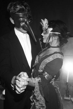 black and white photograph of man and woman in costume holding hands with mask on face