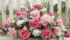 a bouquet of pink and white flowers sitting on top of a wooden bench in front of a picket fence