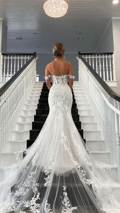 a woman in a white wedding dress standing on stairs with her back to the camera